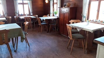 Ein Essbereich mit Holztischen und -stühlen, einem Schrank mit Dekoration und Fenstern mit Vorhängen.