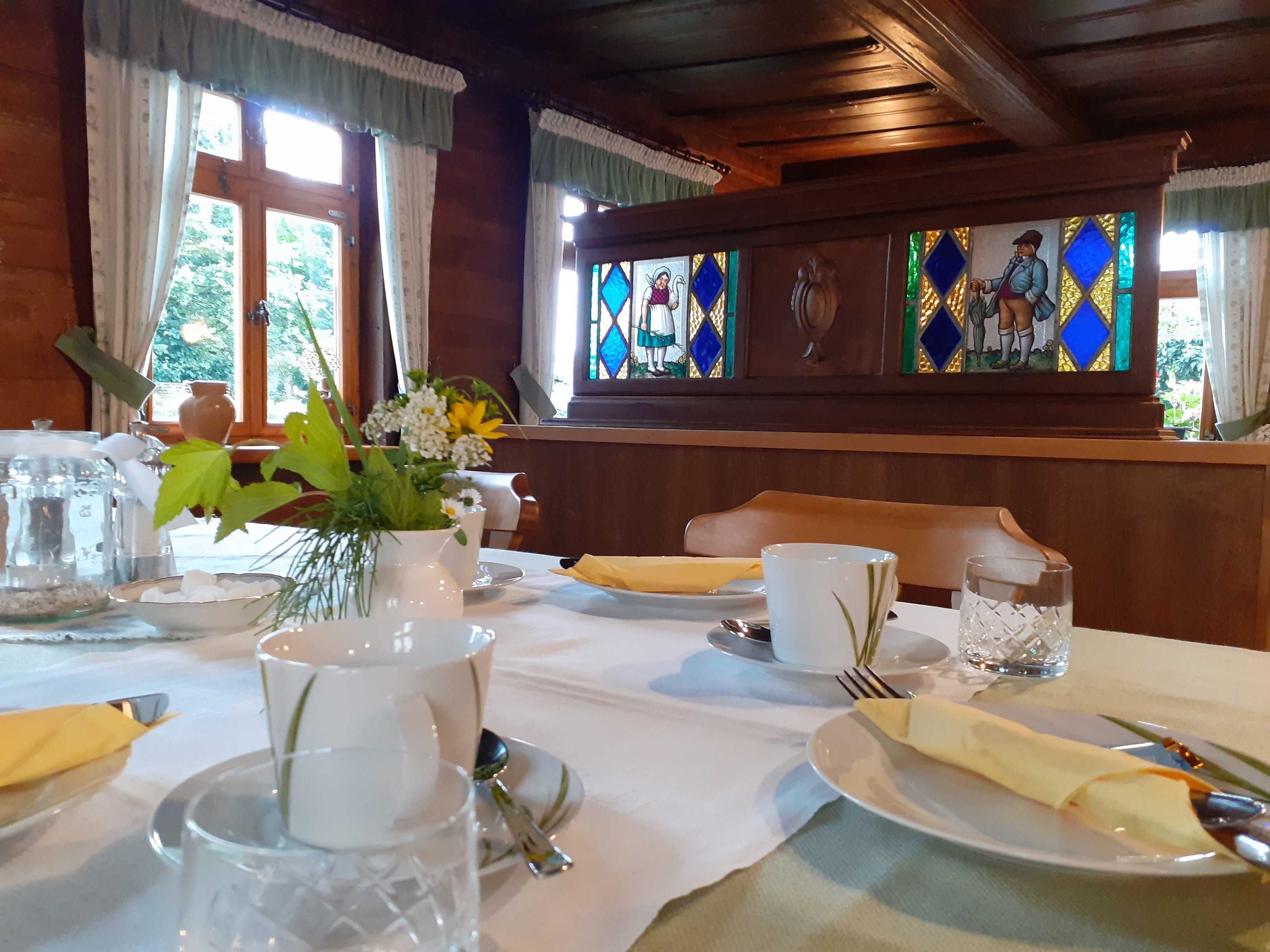 Ein Esstisch ist gedeckt mit Tellern, Besteck und einer Blumenvase.