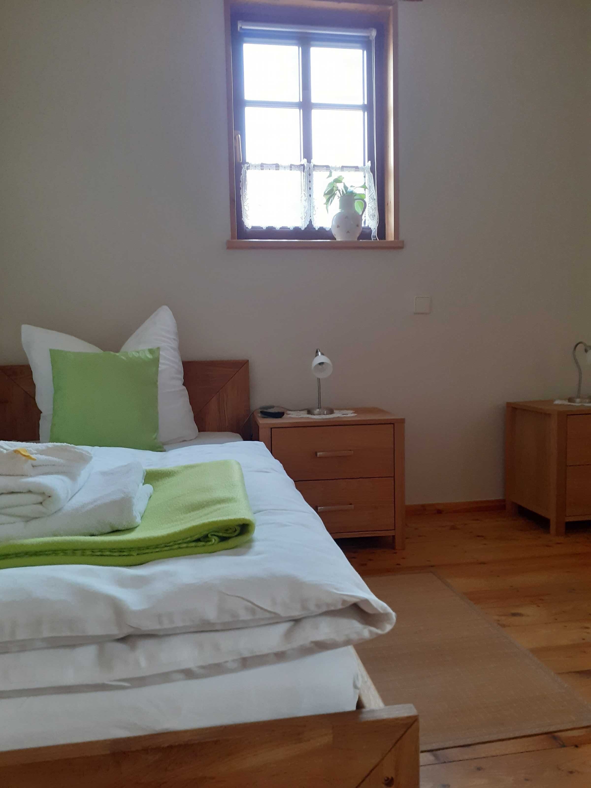 Ein Schlafzimmer mit Bett, Nachttisch, Kommode, einem Fenster mit Ausblick und einer Lampe auf dem Nachttisch.