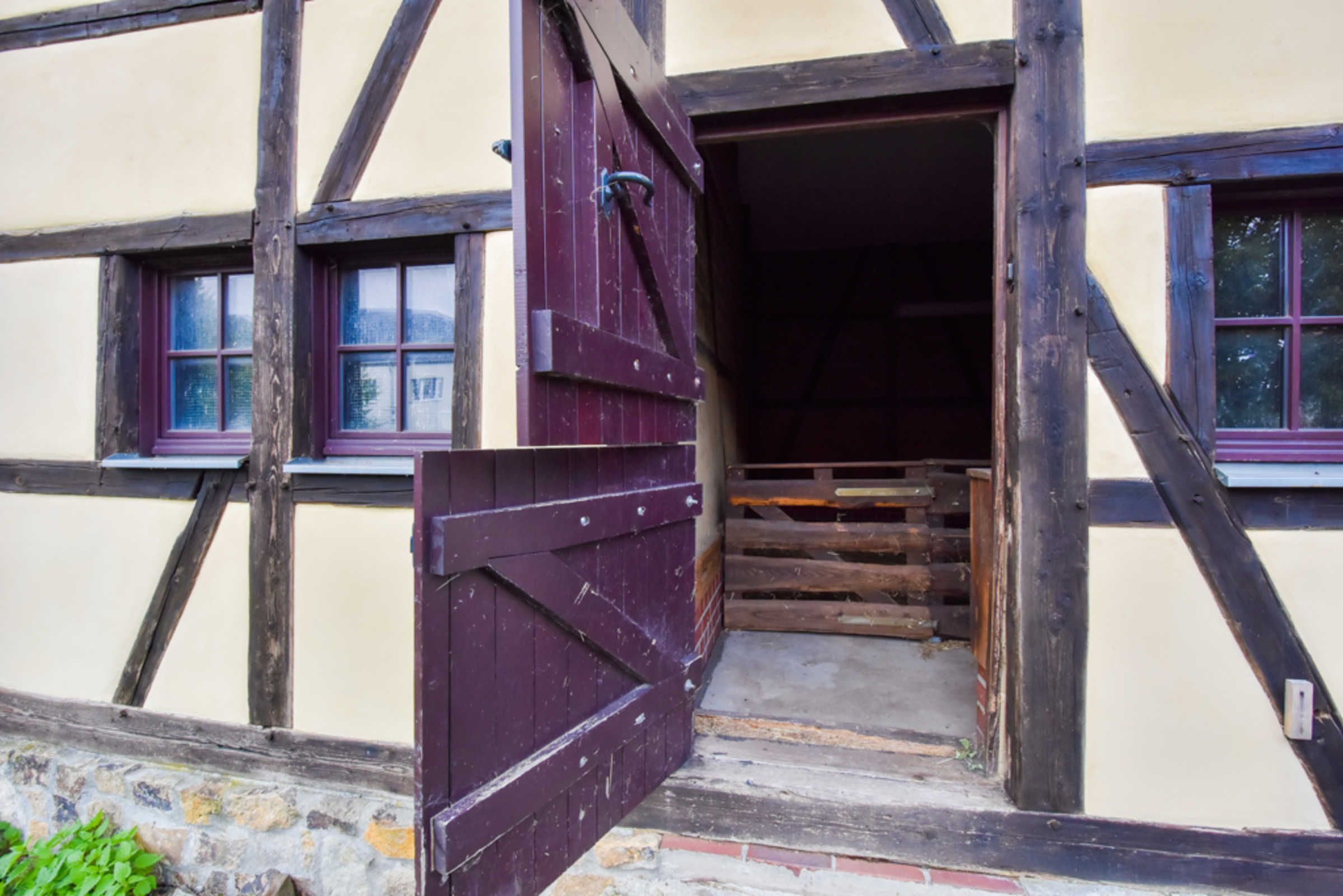 Ein traditionelles Fachwerkhäuschen mit Holztür, Steinwand und Fenster mit Rollo.