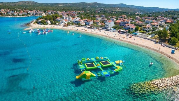 A coastal town with clear blue waters, a sandy beach, and a floating structure. - Apartments Jelena (Rogoznica)