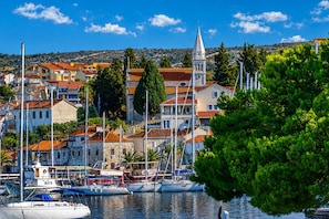 A coastal town with a marina, buildings with red-tiled roofs, and a prominent church steeple. - Apartments Jelena (Rogoznica)
