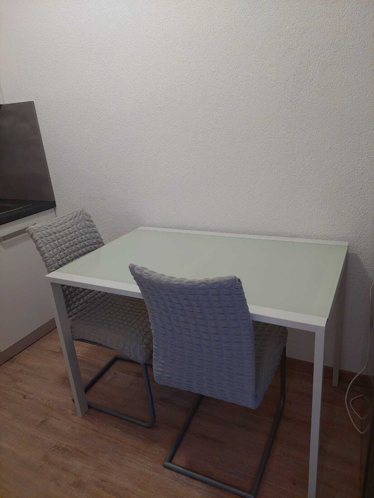 Un pequeño comedor con una mesa blanca y dos sillas.