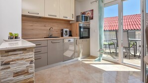 A modern kitchen with a stone accent wall, a built-in oven, and a microwave on the countertop. - Apartments Jelena (Rogoznica)