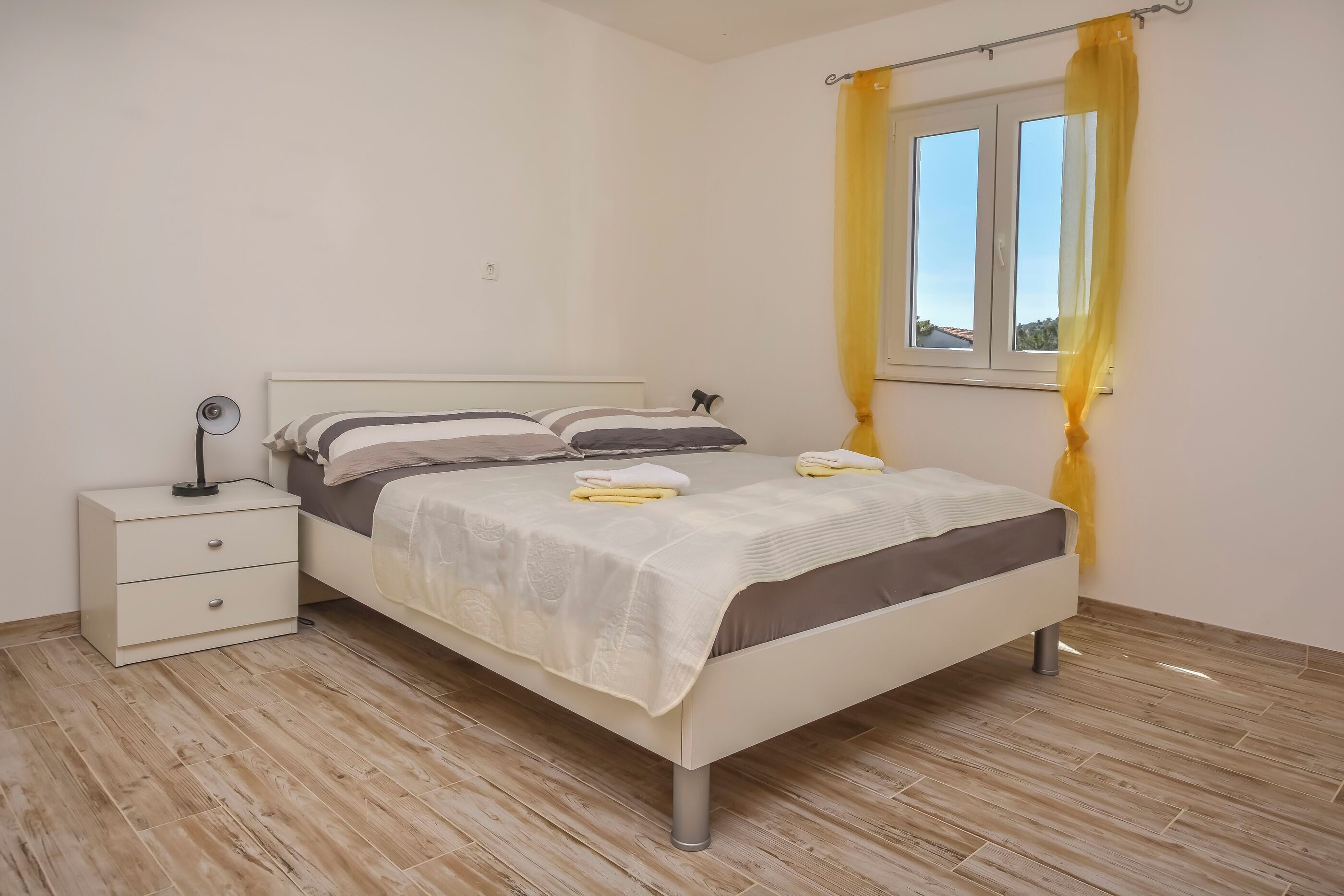 Una camera da letto ordinata con un letto, comodini e una finestra con tende gialle.