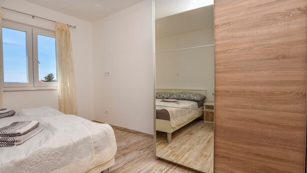 A bedroom with a bed, a bedside table, a mirror, and a wardrobe. - Apartments Jelena (Rogoznica)