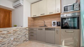 A modern kitchen with a stone backsplash, stainless steel appliances, and wooden cabinets. - Apartments Jelena (Rogoznica)