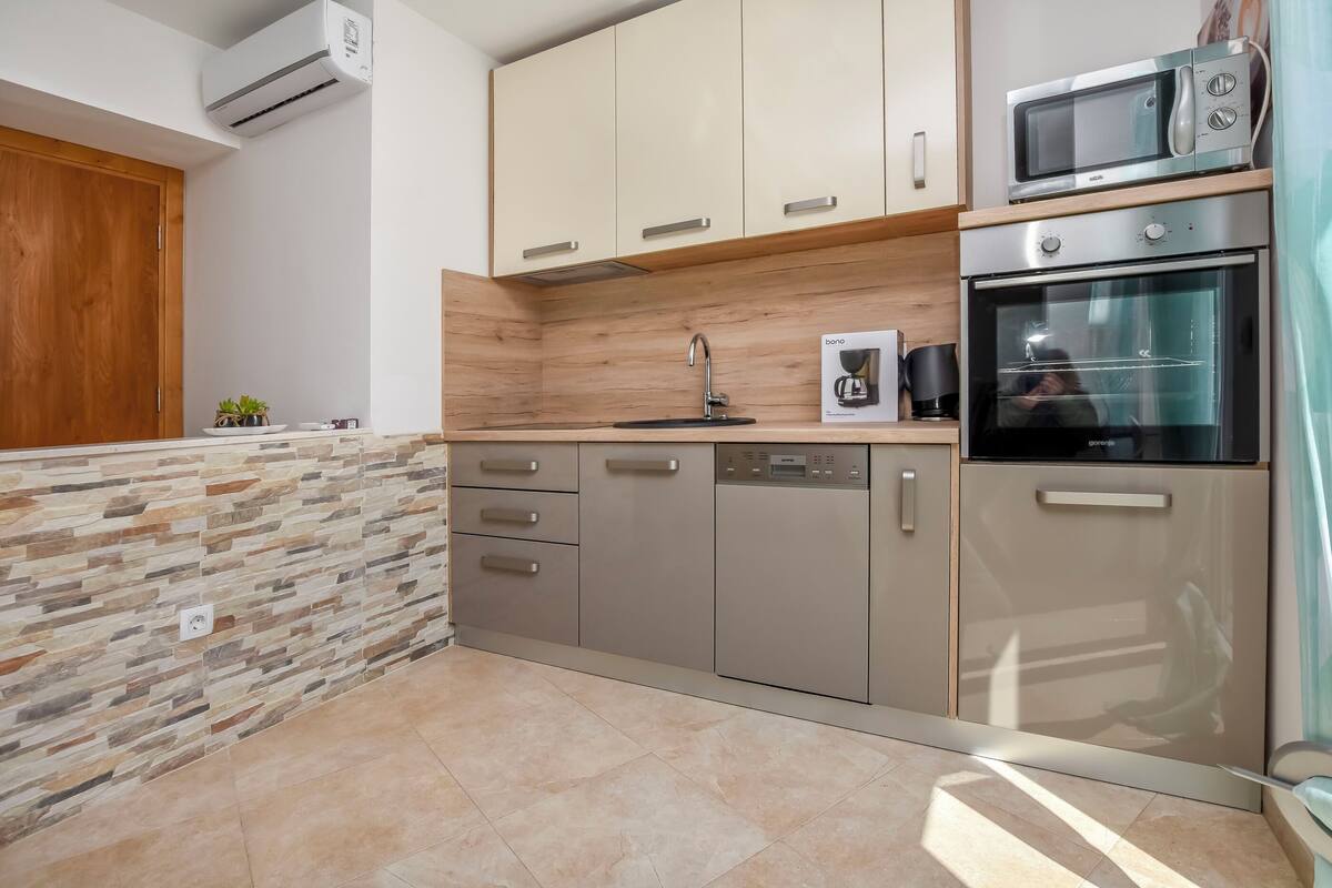 A modern kitchen with a stone backsplash, stainless steel appliances, and wooden cabinets.