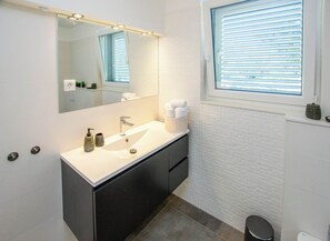 A modern bathroom with a white sink, dark cabinets, a large mirror, and a window with blinds. - House Villa Verdi (Tkon)