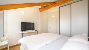 A bedroom with a bed, a TV on a stand, a white chair, and a wardrobe. - House Villa Verdi (Tkon)