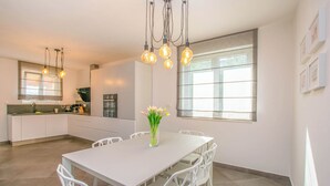 A modern kitchen with white cabinetry, a dining table with chairs, and a vase of flowers. - House Villa Verdi (Tkon)