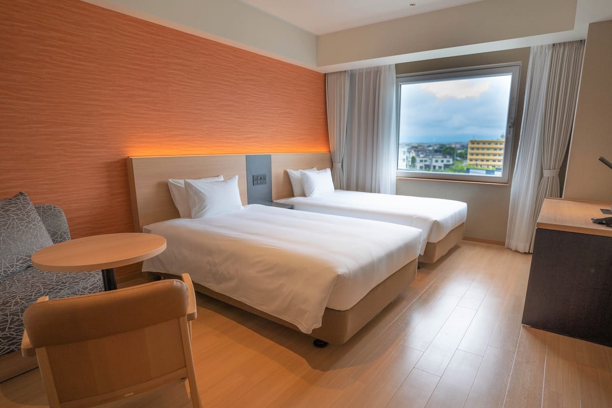A hotel room with two beds, a small table, a chair, and a desk with a computer.