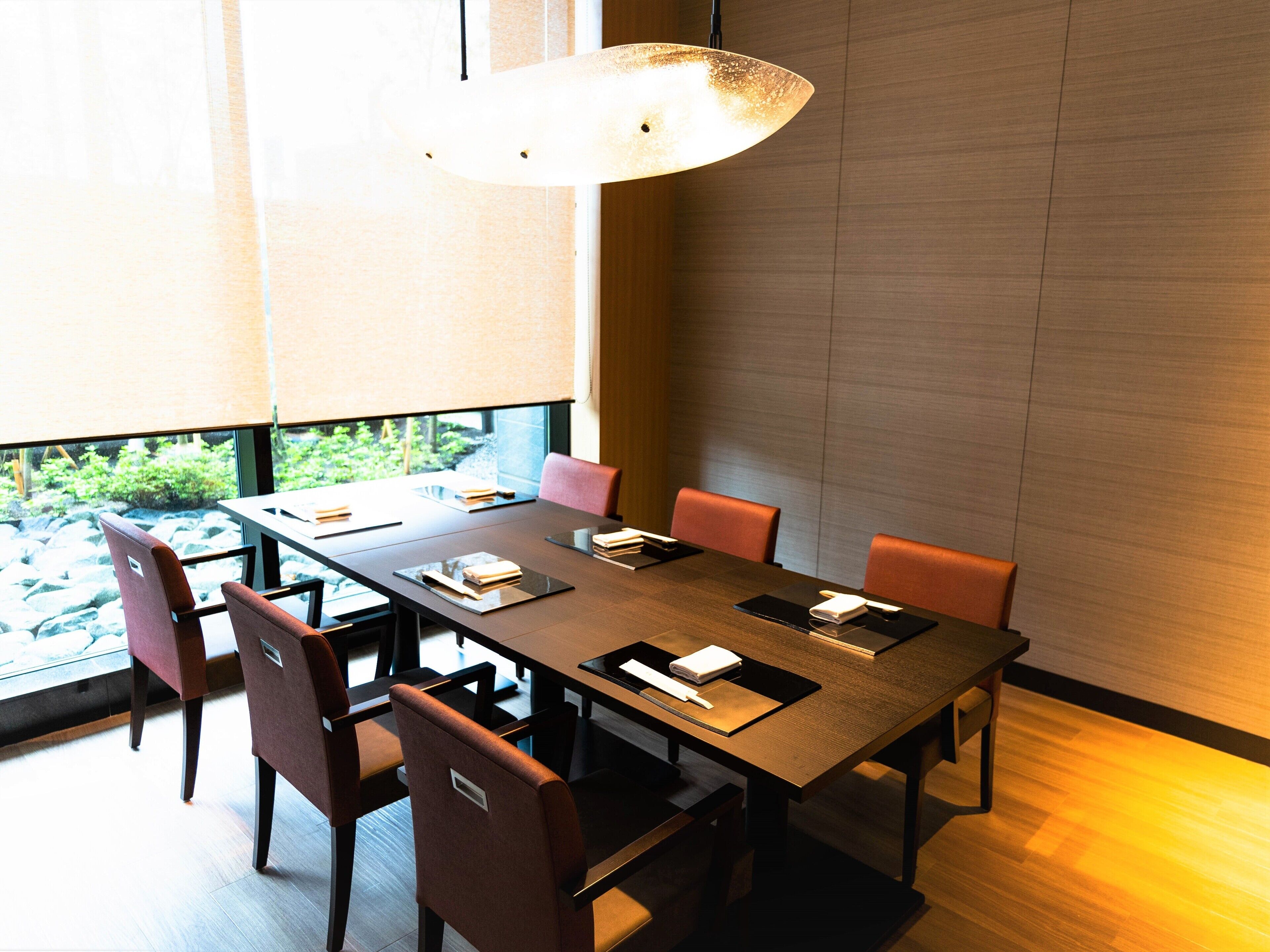 A conference room with a long table, six chairs, and a hanging light fixture.