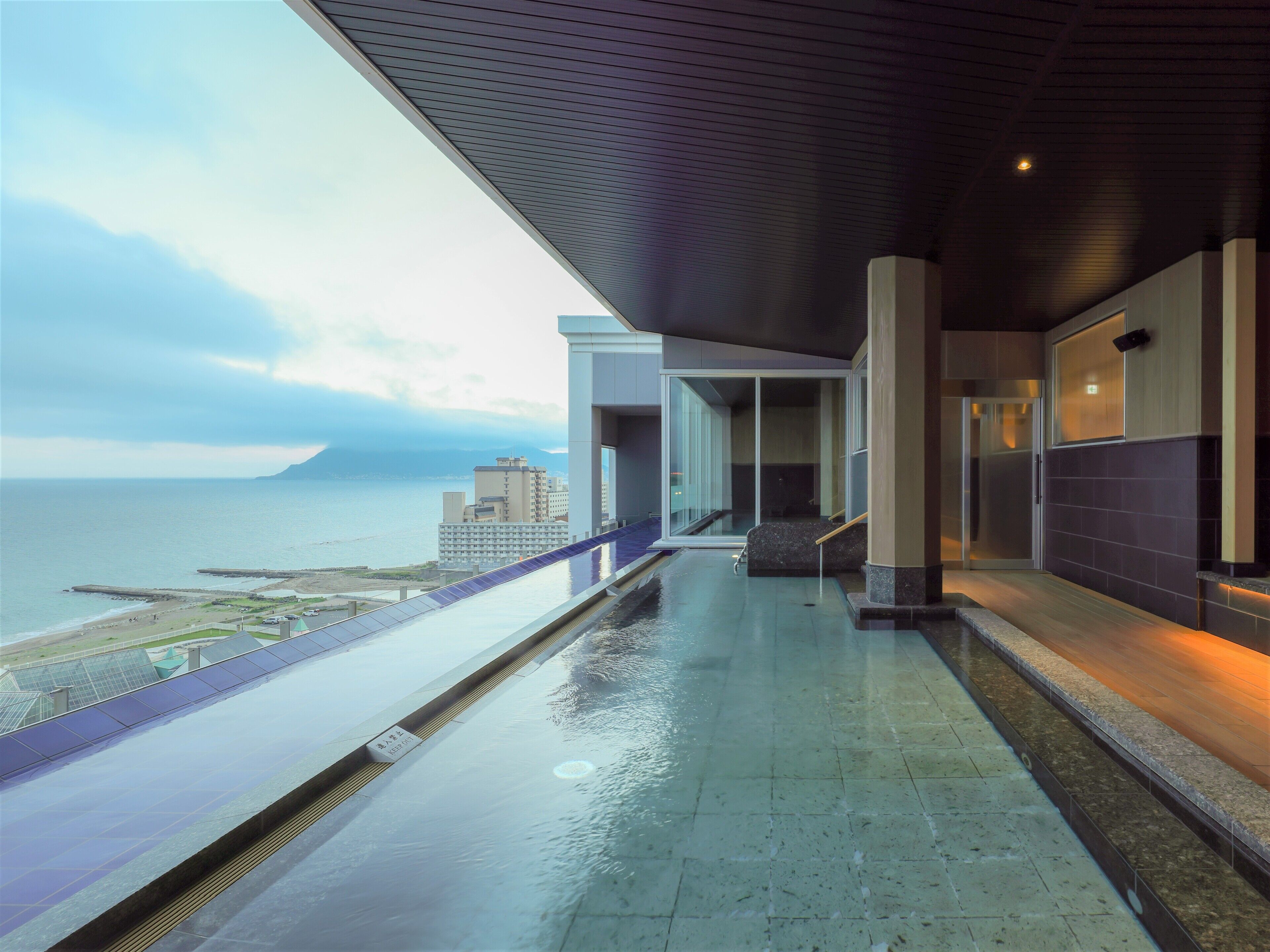 A modern building with a glass facade overlooking a body of water and distant mountains.