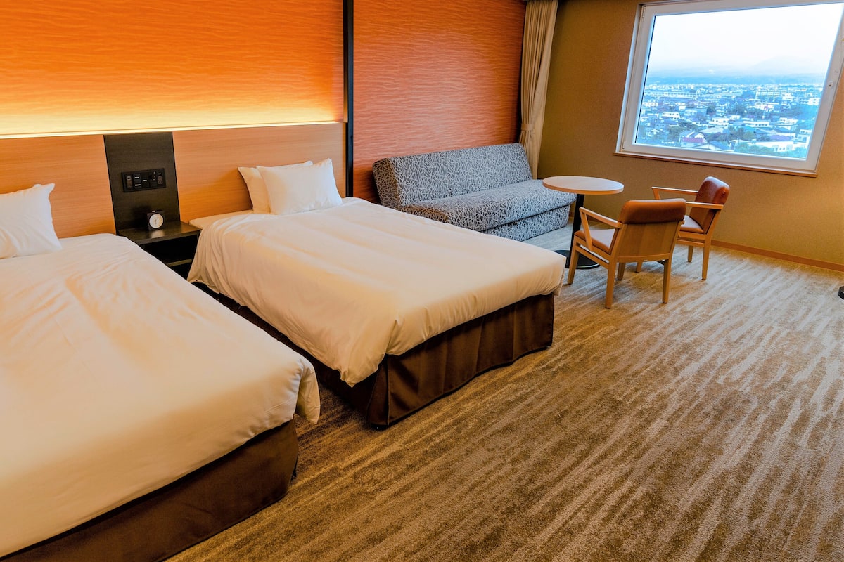A hotel room with two beds, a sofa, a small table, and a chair.