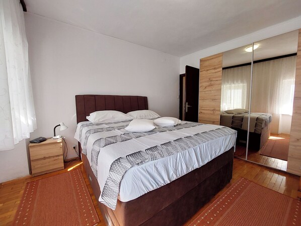 A neatly arranged bedroom with a large bed, a bedside table with a lamp, and a mirror on the wall. - Apartment Klara (Dramalj)