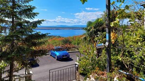 A parking area with a blue car, surrounded by trees and a view of a lake and mountains. - Apartment Klara (Dramalj)