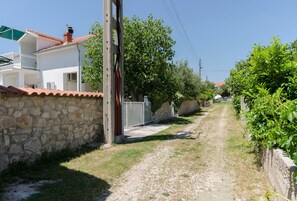 A narrow gravel path flanked by stone walls and greenery, leading to a white building with a red-tiled roof and a balcony. - Apartments Mirjana Blue Beach (Vodice)