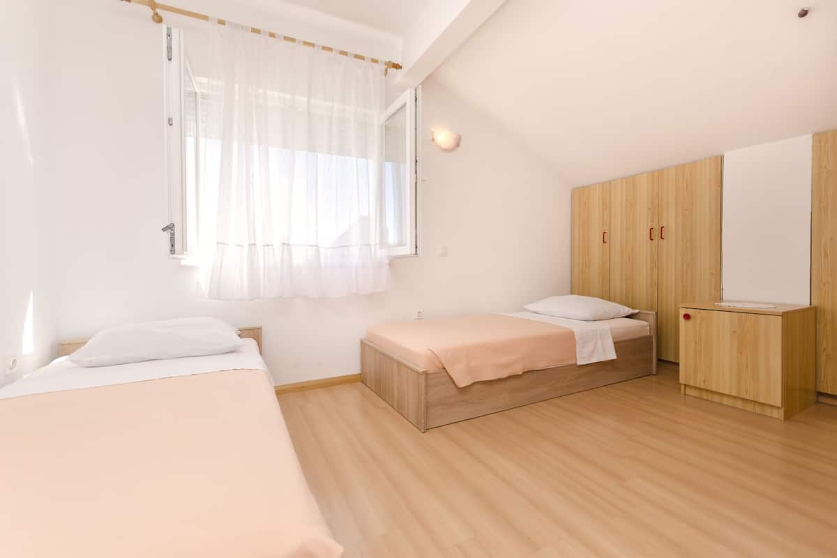 Ein Schlafzimmer mit zwei Betten, einem Holzschrank und einem Fenster mit durchsichtigen Vorhängen.
