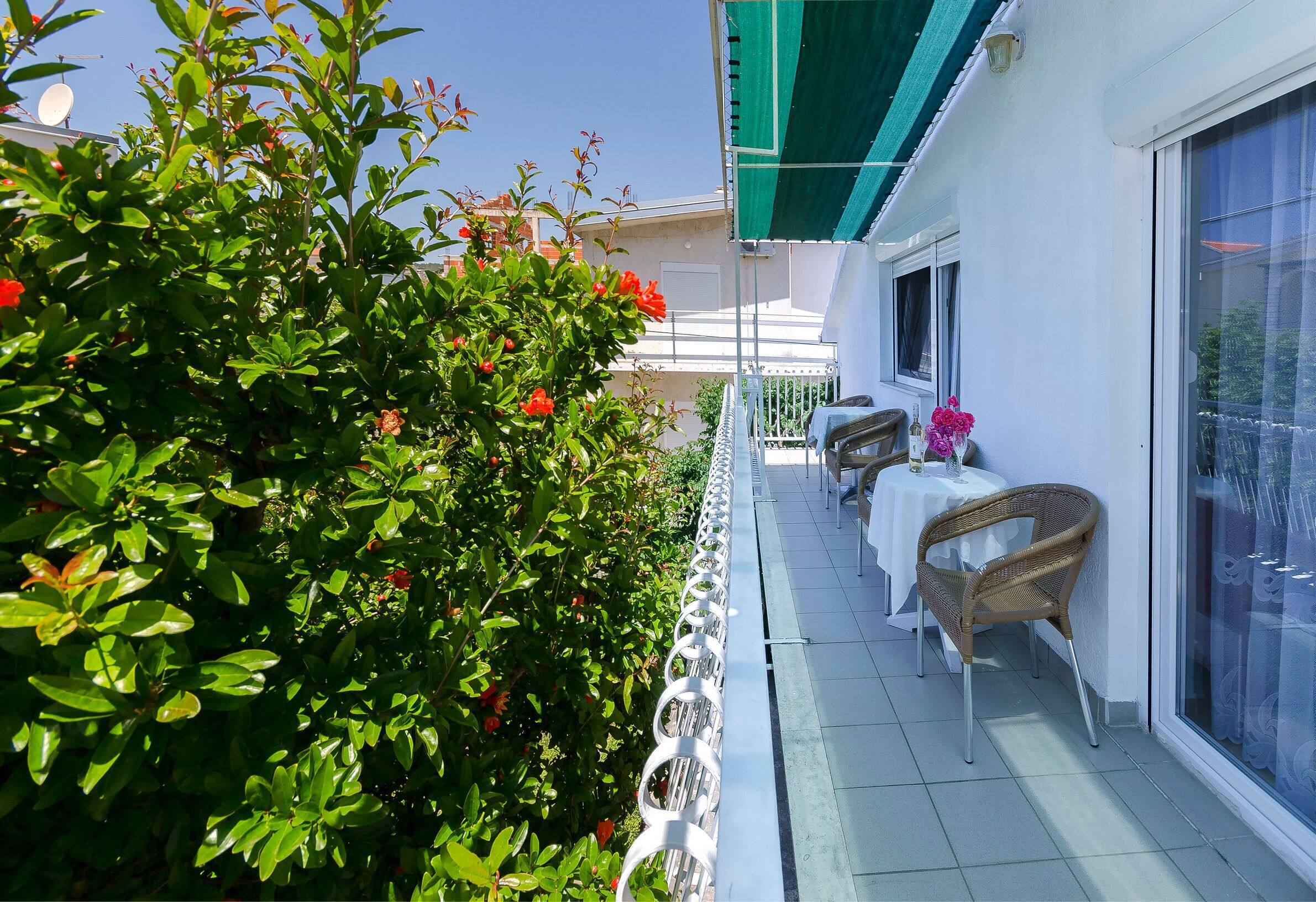 A balcony with a white railing, a wicker chair, and a table with a white tablecloth.