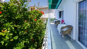 Un balcon avec une balustrade blanche, une chaise en osier et une table recouverte d’une nappe blanche.