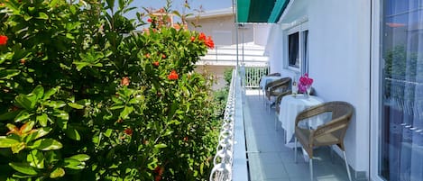 A balcony with a white railing, a wicker chair, and a table with a white tablecloth.