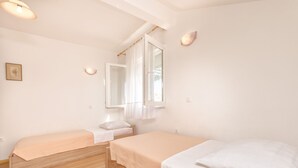 Une chambre avec deux lits simples, une fenêtre avec des rideaux, un miroir et un luminaire.