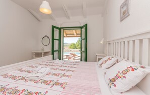 A bedroom with a bed, a small table, a mirror, and an open door leading to an outdoor area with a table and chairs. - Villa Ibis (Vrana)