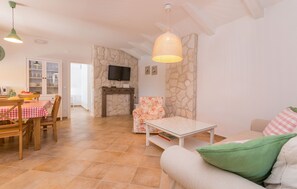 A cozy living room with a sofa, a dining table with chairs, a television, and a stone wall. - Villa Ibis (Vrana)