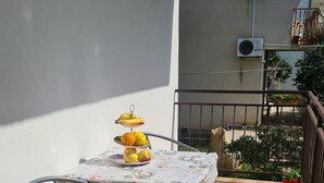 Eine kleine Terrasse im Freien mit Tisch und Stühlen, einem Blumentopf und Blick auf ein Gebäude im Hintergrund.