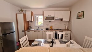 Eine kleine Küche mit Kühlschrank, Herd, Mikrowelle und Spüle. Ein Esstisch für zwei Personen ist gedeckt mit Tellern und Gläsern.