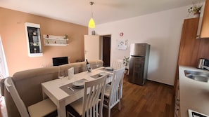 Une cuisine moderne dotée d’un réfrigérateur encastré, un coin repas avec une table dressée pour deux personnes et un coin salon confortable avec un canapé.