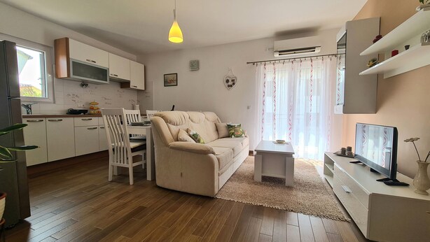 Ein modernes Wohnzimmer mit einem beige Coloured Sofa, einem kleinen Couchtisch und einem Fernseher. Es gibt eine Küchenzeile mit weißen Schränken und einer Mikrowelle.