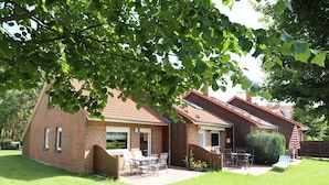 Een tweelaags bakstenen huis met een patio, tuinmeubilair en een kleine tuin.