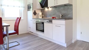 Een moderne keuken met witte kasten, roestvrijstalen apparatuur en een rode stoel.