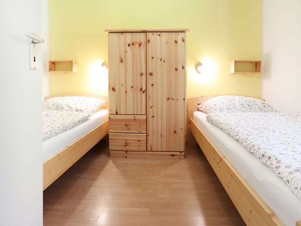 A bedroom with two single beds, a wooden wardrobe, and bedside lamps.