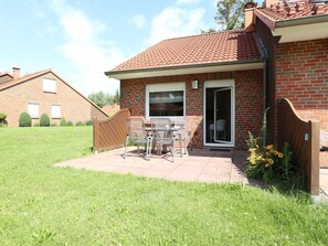 A brick house with a tiled roof, a patio with a table and chairs, and a small garden area.