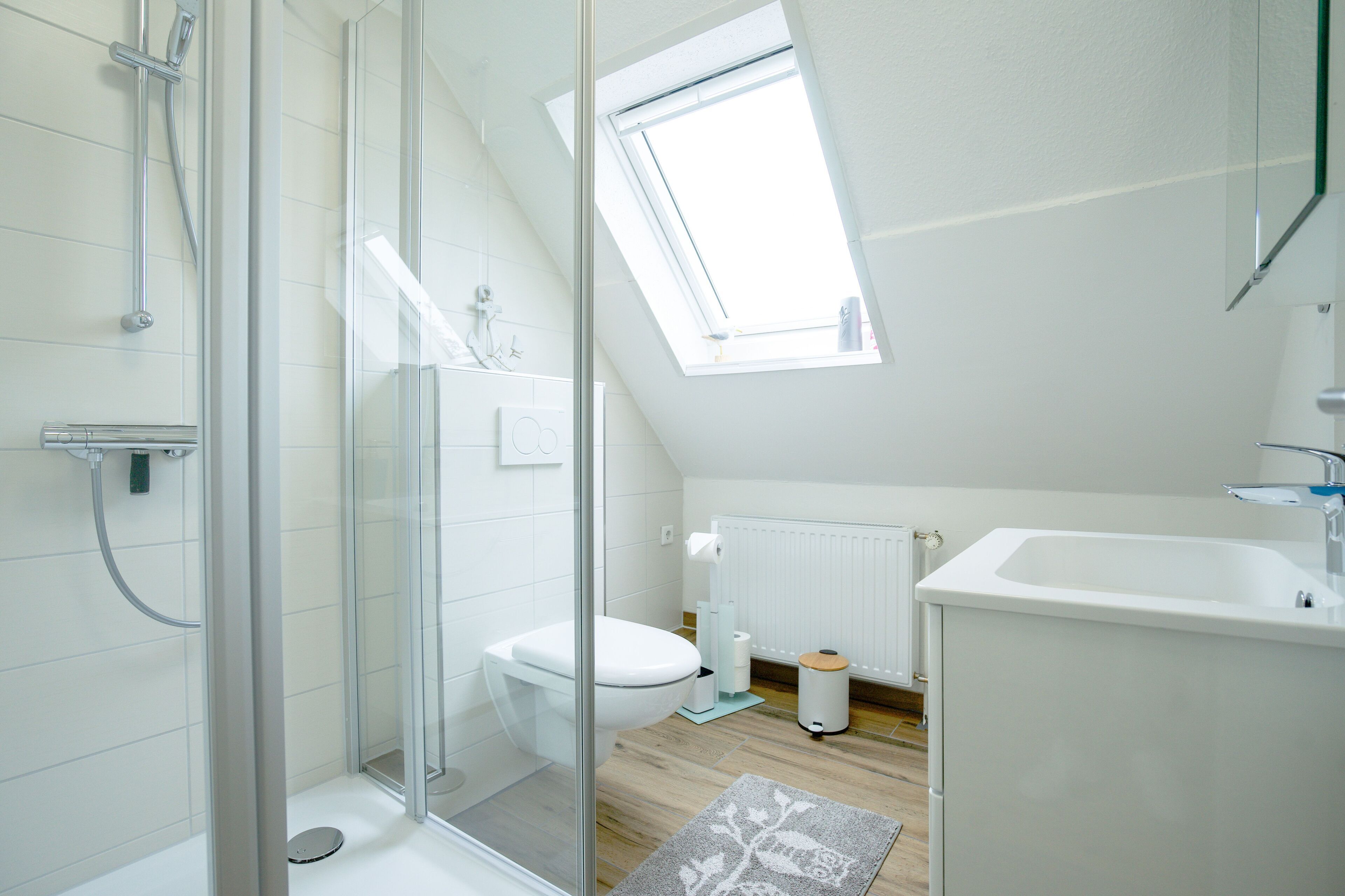 Et moderne badeværelse med brusekabine i glas, ovenlys, toilet i hvidt og en vask.