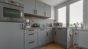A modern kitchen with grey cabinets, a built-in oven, a coffee machine, and a microwave.