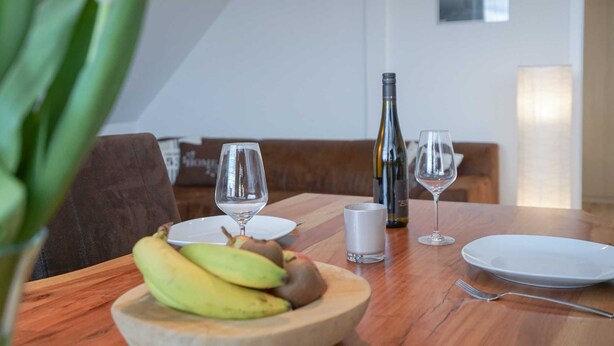 A dining table with a bowl of fruit, two wine glasses, a wine bottle, and a candle.