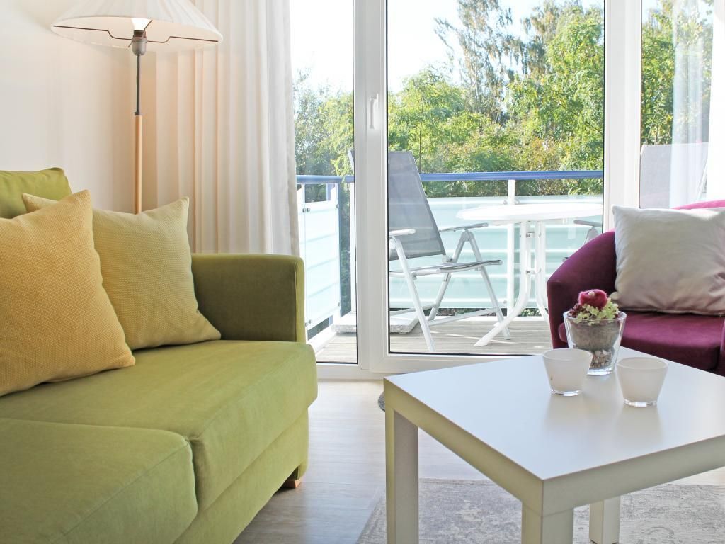Et værelse med en grøn sofa, et hvidt bord og en balkon med en stol og et bord.