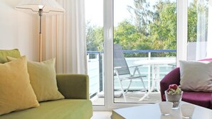 Une pièce avec un canapé vert, une table blanche et un balcon équipé d’une chaise et d’une table.