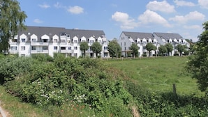 Une rangée d’immeubles d’appartements modernes, dotés d’un toit plat, entourés d’un champ verdoyant et d’une végétation dense.
