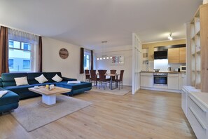A modern living room with a sofa, coffee table, and dining area. There is a kitchen with white cabinets and a microwave. - Seebach Whg. S01, Deutschland (Ostseebad Boltenhagen)