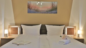 A hotel room with a large bed, two bedside tables with lamps, a painting on the wall, and a book on the bed. - Seebach Whg. S01, Deutschland (Ostseebad Boltenhagen)