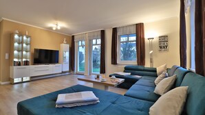 A modern living room with a large teal sofa, a flat-screen TV, and a bookshelf. - Seebach Whg. S01, Deutschland (Ostseebad Boltenhagen)