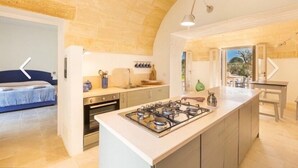 A compact kitchen with a central island, a dining area with a table and chairs, and a bedroom with a bed. - Villa Lusso (salve)