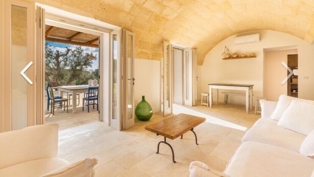 A spacious living area with a stone ceiling, a wooden coffee table, white sofas, and a dining area with a table and chairs. - Villa Lusso (salve)