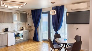 A modern kitchen with a built-in oven, a white refrigerator, and a dining area with a round table and four chairs. - Dream Mamaia North (Navodari)