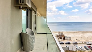 A balcony with wicker furniture, a view of the beach, parked cars, and a clear sky. - Dream Mamaia North (Navodari)